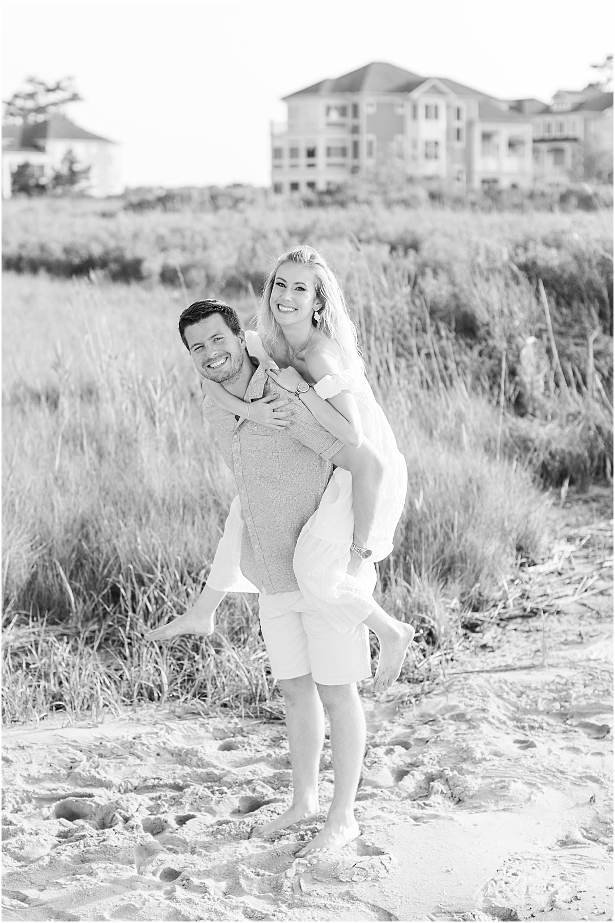 Black and white photo of Don giving Val a piggy back ride during their beach engagement.