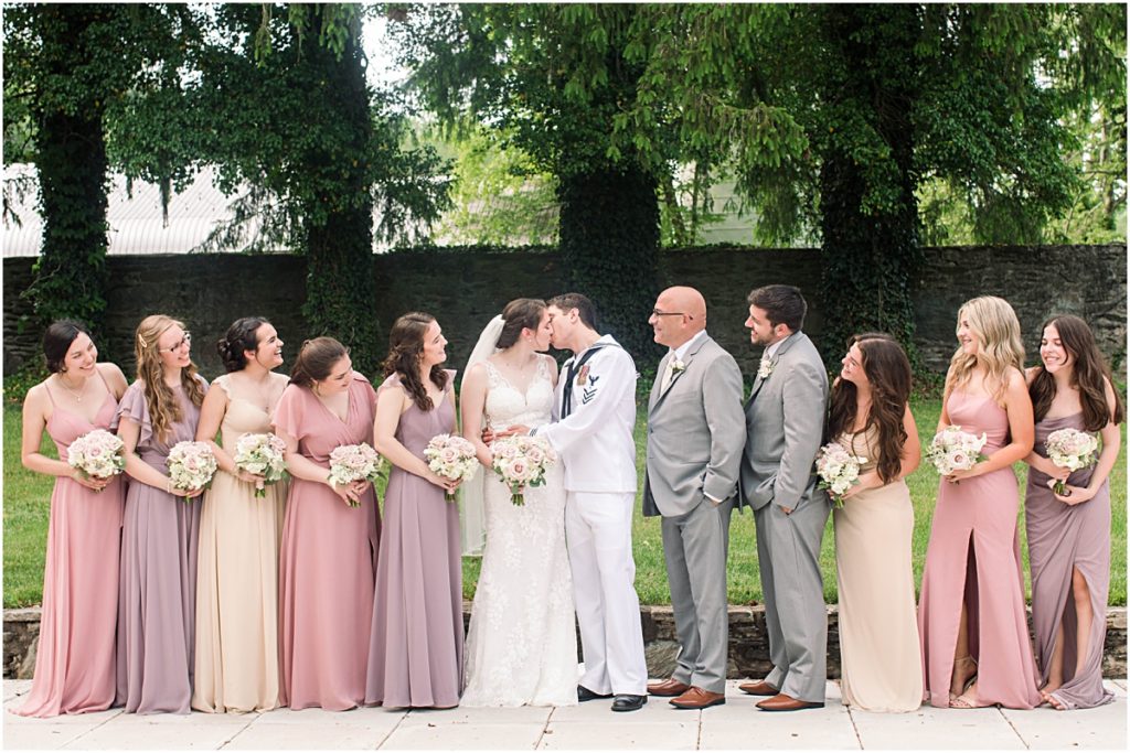 The couple kissing while the bridal party watches and smiles. Wedding photography in Maryland done by Ashley.