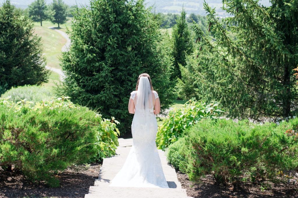 katie facing away from the camera surrounded by greenery on her Cotoctin Hall Wedding at the Musket Ridge Golf Club in Maryland 