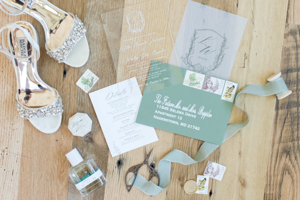 detail image of wedding details that includes invitations to the Cotoctin Hall Wedding, bridal shoes, perfume and sage green ribbon