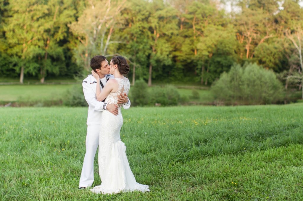 A bride and groom kissing in a field on their wedding day.