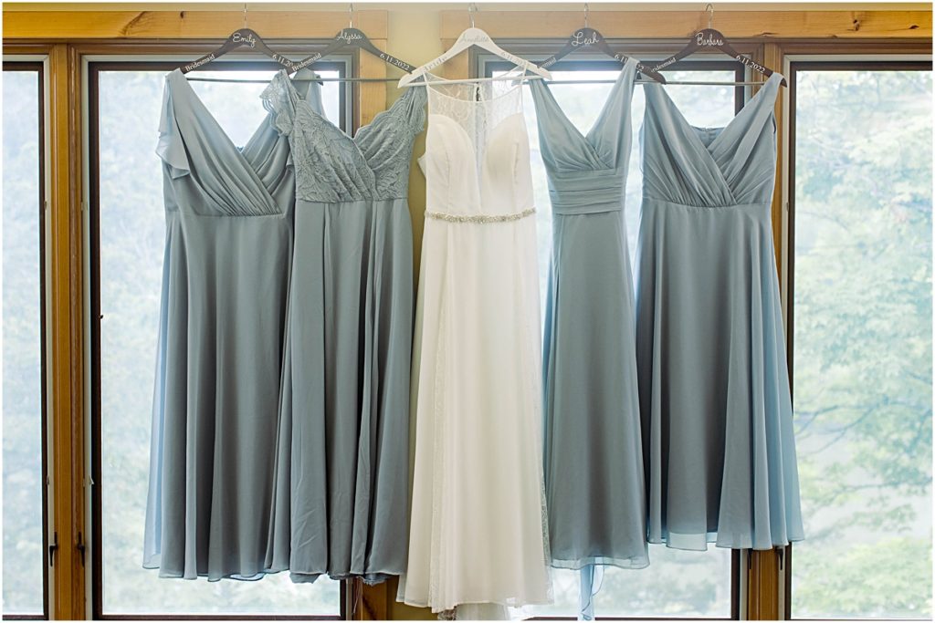 Detail photo of the bride's wedding dress hanging with her bridesmaids dresses in the window of Poor Farm House Park.