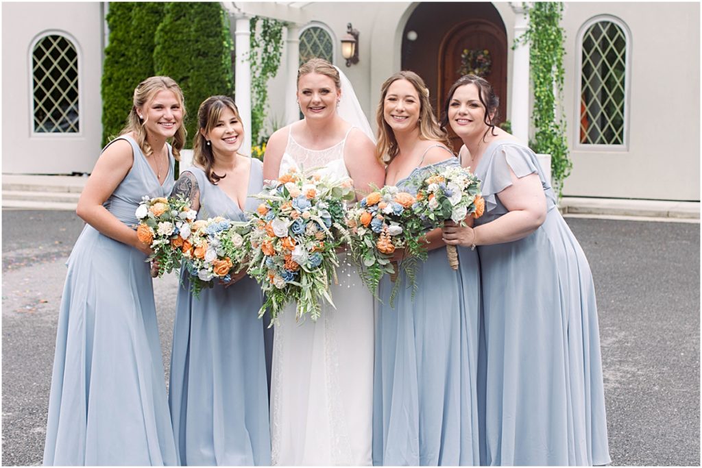 Anneliese and her bridesmaids smiling as they lean in together in front of the house at Poor Farm House Park.