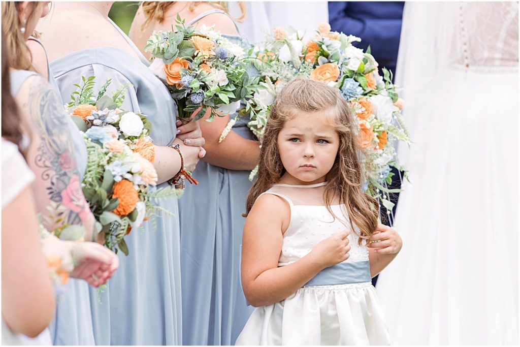 A detail photo of the flower girl looking off in the distance as she stands in front of the bridesmaids during a wedding ceremony.