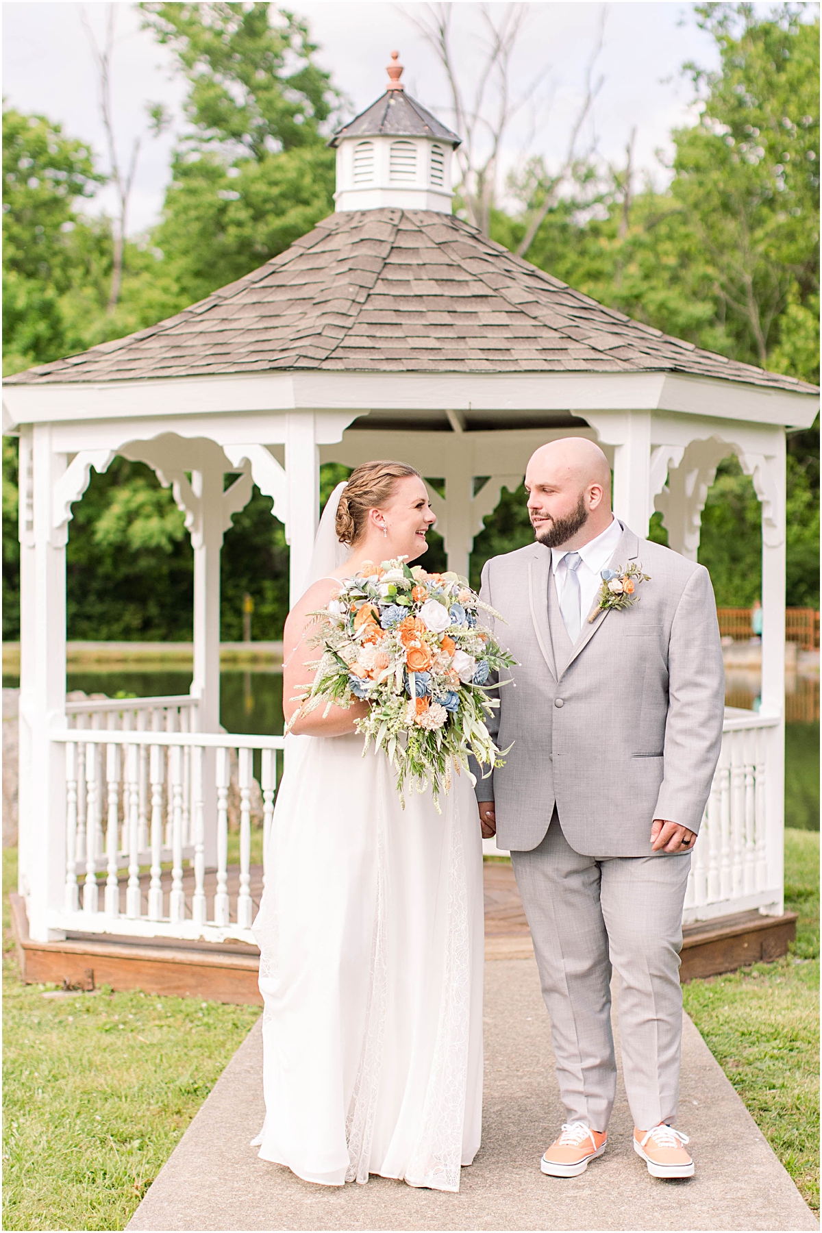 Anneliese and Alec smiling at each other while they stand in front of a gazebo on their wedding day.